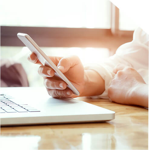 pessoa com celular na mão em frente a um computador